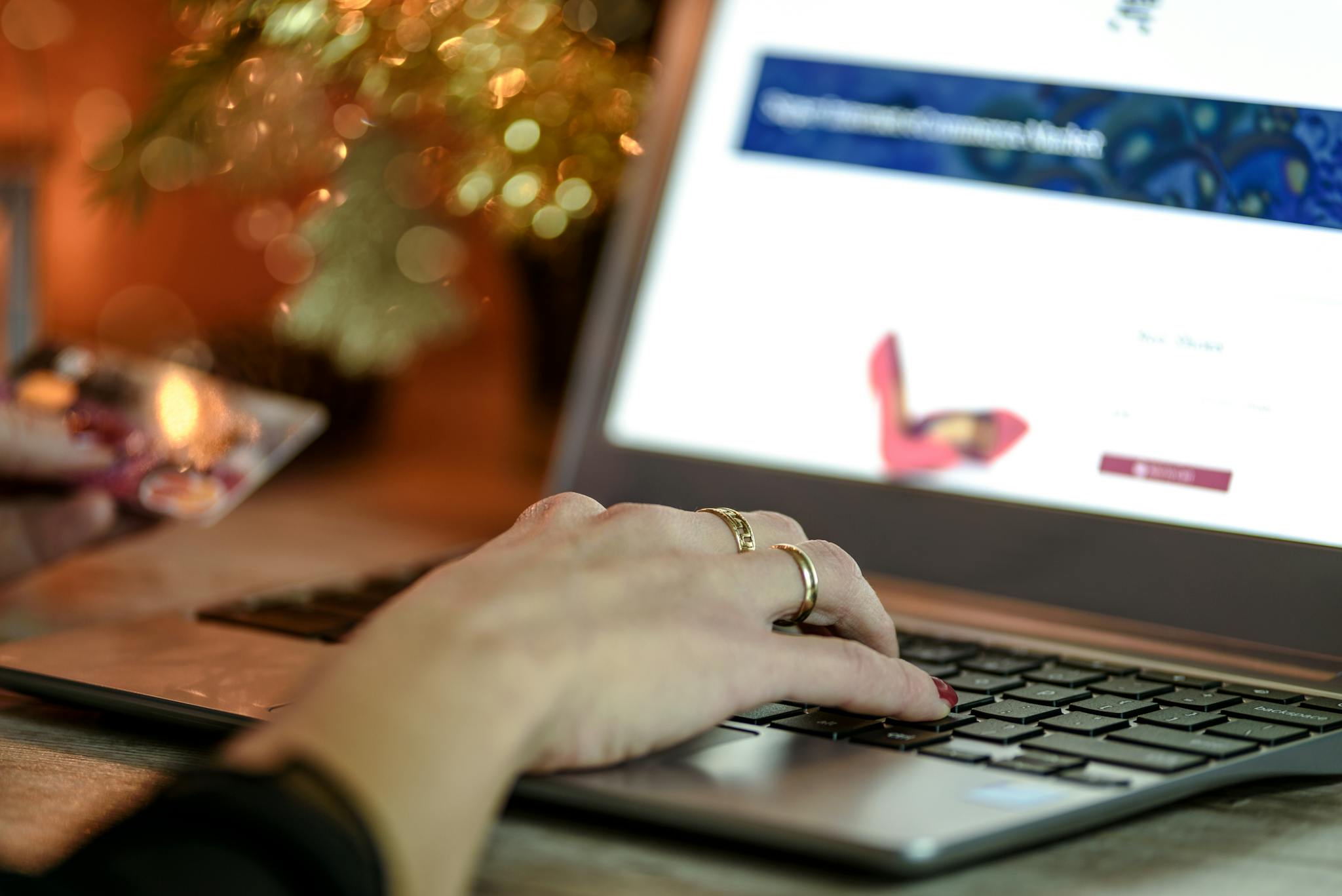 Close-up of a hand using a laptop keyboard while holding a credit card, symbolizing online shopping.